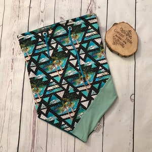 Könnte beinhalten: Eine Kordelzugtasche mit einem geometrischen Muster in Schwarz und Weiß, das Palmen und blaue Wellen zeigt. Die Tasche hat ein türkisfarbenes Futter und blaue Kordeln.