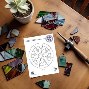 Peut inclure: Sc&egrave;ne d'atelier avec un patron de capteur solaire en forme de fleur g&eacute;om&eacute;trique, mesurant 7" x 7" (17,78 cm x 17,78 cm). Des morceaux de vitrail color&eacute;s et un fer &agrave; souder sont dispos&eacute;s autour. Un pot de succulente est &eacute;galement visible.