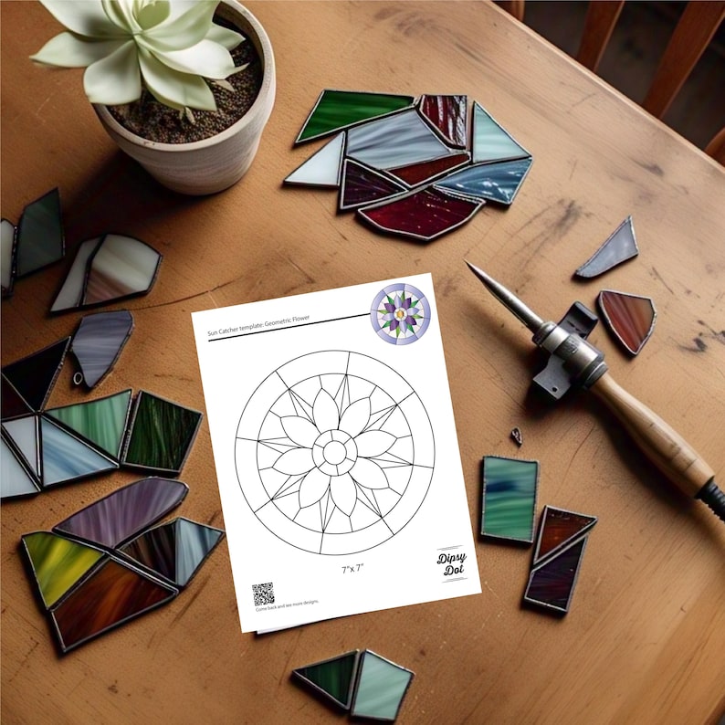 Peut inclure: Sc&egrave;ne d'atelier avec un patron de capteur solaire en forme de fleur g&eacute;om&eacute;trique, mesurant 7" x 7" (17,78 cm x 17,78 cm). Des morceaux de vitrail color&eacute;s et un fer &agrave; souder sont dispos&eacute;s autour. Un pot de succulente est &eacute;galement visible.