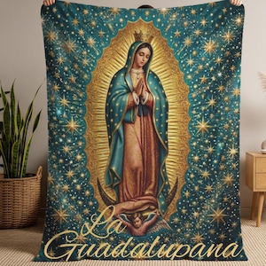 May include: A teal and gold blanket featuring an illustration of the Virgin of Guadalupe. The image includes a halo, stars, and the text "La Guadalupana" in gold script. The blanket is held up in front of a neutral background.