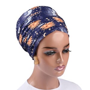 May include: A blue turban with a gold and white sun and moon pattern. The turban is worn by a person with brown skin and dark hair.