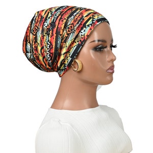 May include: A black, orange and blue patterned turban with geometric designs. The turban is worn on a mannequin with a white shirt.