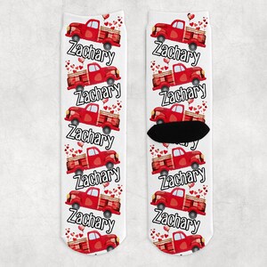 May include: A pair of white socks with a red truck and hearts pattern. The truck is carrying hearts and the socks have the name "Zachary" repeated on them.