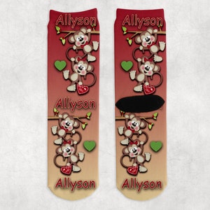 May include: A pair of socks with a gradient design from red to yellow. The socks feature a repeating pattern of monkeys holding hearts and the name "Allyson" printed on each sock.