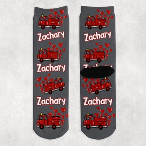 May include: A pair of gray crew socks with a red fire truck and hearts pattern. The socks have the name "Zachary" repeated on them.