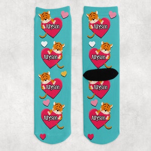May include: A pair of blue socks with a repeating pattern of pink hearts, yellow stars, and cartoon tigers holding pink hearts with the name "Allyson" printed on them.