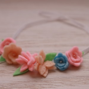 May include: A white headband with pink, peach, and blue felt flowers. The flowers have a center bead.
