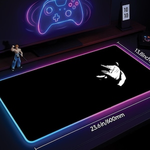 May include: Black rectangular gaming mouse pad with a white anime character design. The pad has a glowing blue and pink border and measures 23.6 inches by 13.8 inches. A neon-lit controller graphic is visible in the background.