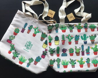 May include: Two white canvas tote bags with cactus designs. The bag on the left has a cactus design around the edge and the text "PERMANO" in the center. The bag on the right has a repeating cactus design.