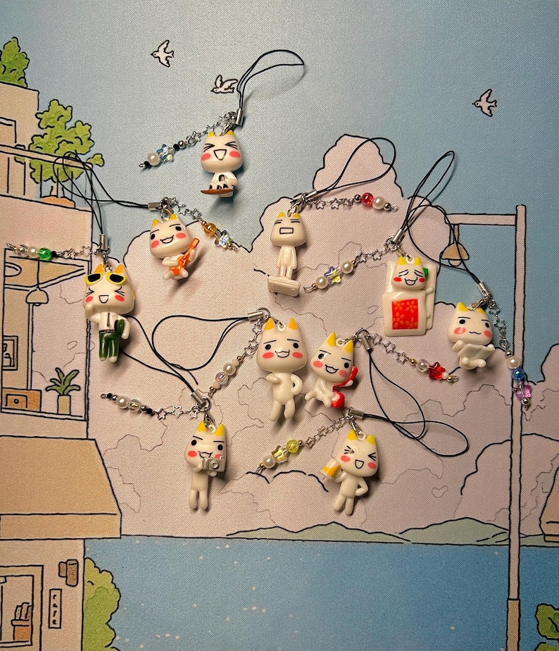 Puede incluir: Una colecci&oacute;n de 10 dijes de tel&eacute;fono de personajes de dibujos animados blancos y amarillos con diferentes expresiones y accesorios. Los dijes est&aacute;n unidos a cadenas negras y plateadas con cuentas blancas.