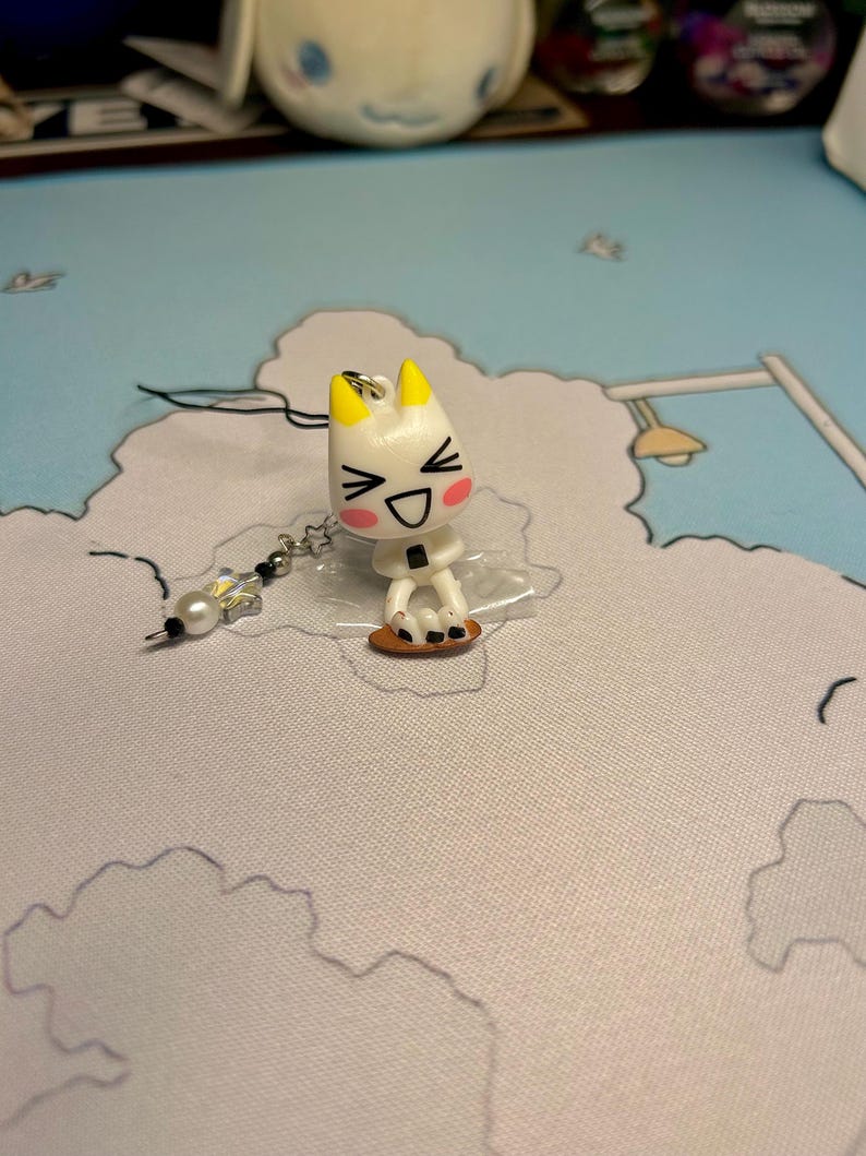 Puede incluir: Encanto de personaje de dibujos animados blanco y amarillo con una cara sonriente y ojos negros. El encanto est&aacute; unido a una cadena plateada con una cuenta de cristal transparente.