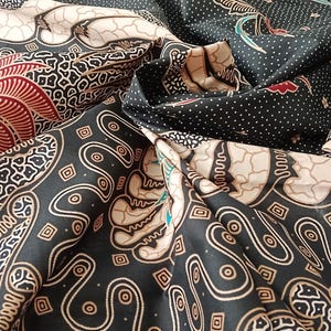 Puede incluir: Primer plano de tela estampada con una variedad de diseños. La tela presenta una mezcla de patrones florales y geométricos negros, blancos y rojos. La tela está doblada, mostrando los diferentes patrones y texturas.