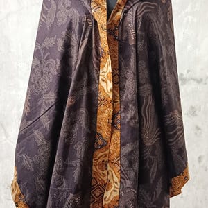 May include: A dark brown shawl with a floral pattern and a contrasting gold border. The shawl is draped over a mannequin, showcasing its design and texture. The text "LKG+" is visible in the upper right corner.