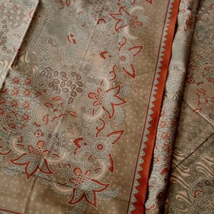 May include: A close-up of a fabric with a brown and white floral pattern. The fabric has a red border.