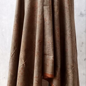 May include: A brown shawl with a paisley pattern and orange trim. The shawl is draped over a mannequin.