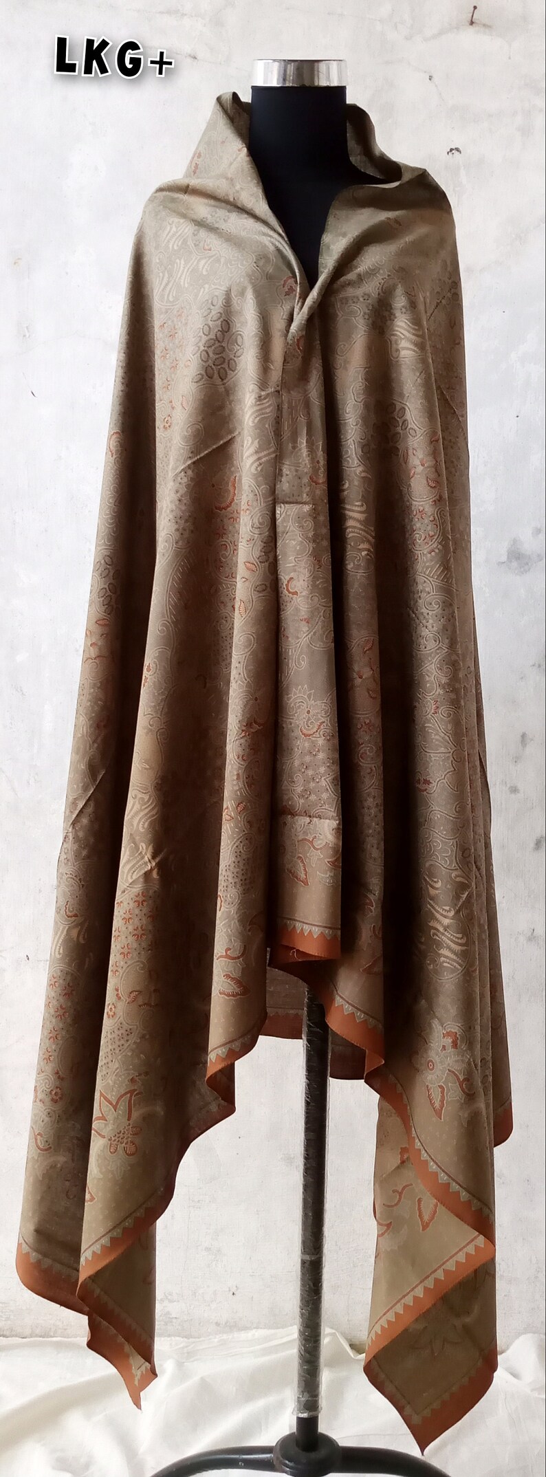 May include: A brown shawl with a paisley pattern and orange trim. The shawl is draped over a mannequin.