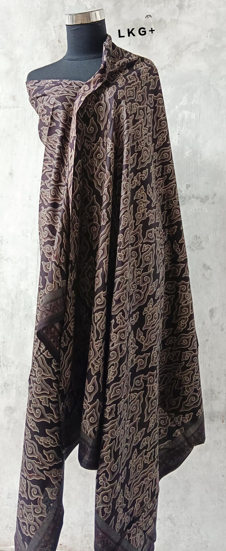 May include: A brown and beige patterned fabric scarf with a repeating cloud design. The scarf is draped over a mannequin.