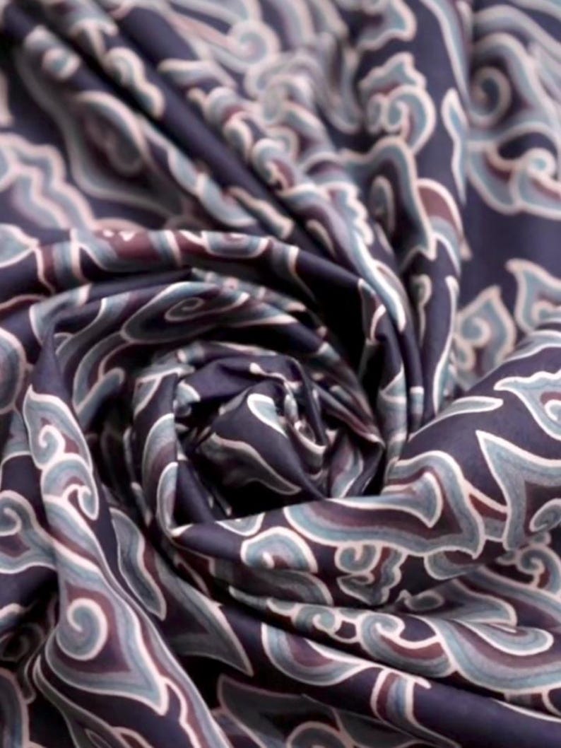 May include: Close-up of a dark blue fabric with a swirling pattern of white and light blue. The fabric has a soft, silky texture.