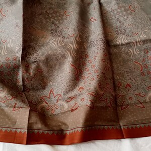 May include: A brown fabric with a white and red floral pattern. The fabric has a brown border with a red trim.