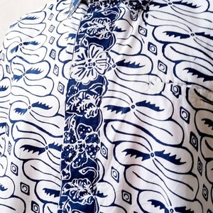Puede incluir: Una camisa de botones con estampado blanco y azul con un diseño floral en la parte delantera. La camisa tiene cuello y cierre de botones. El texto "LKG+" es visible en el cuello.