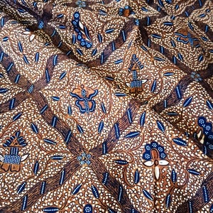 Può includere: Tessuto marrone con un motivo blu e bianco. Il motivo presenta intricati motivi floreali e forme geometriche.
