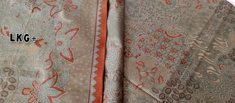 May include: A close-up of two pieces of fabric with a brown and green patterned design. The fabric has a red border and the text "LKG+" is visible in the top left corner.
