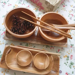 May include: A set of wooden bowls and trays, ideal for serving meals or snacks. The set includes two large bowls, two small bowls, and two rectangular trays. The bowls are made from natural wood and have a smooth finish. The trays are also made from wood and have a natural finish.