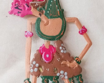 May include: A hand-painted wooden puppet with a green, pink and brown colour scheme. The puppet is a traditional Indonesian shadow puppet, known as a wayang kulit. The puppet is in a standing pose with its arms outstretched. The puppet has a crown and a long, flowing skirt.