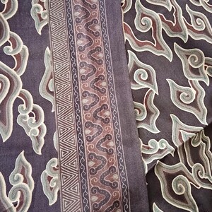 May include: A close-up of a dark brown fabric with a repeating pattern of stylized clouds in shades of green, brown, and white. The fabric has a border with a geometric pattern of triangles and a repeating pattern of stylized clouds.