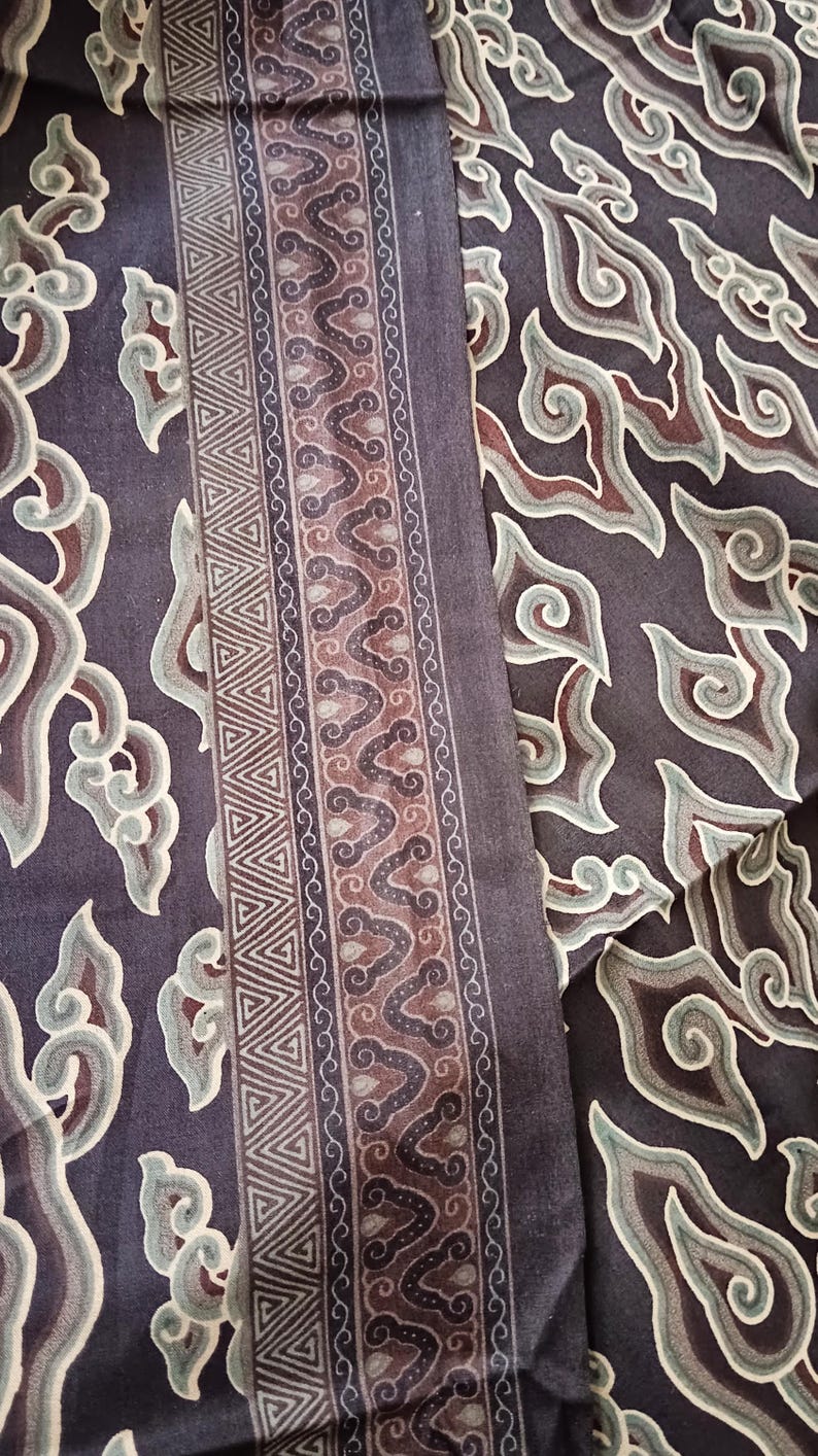 May include: A close-up of a dark brown fabric with a repeating pattern of stylized clouds in shades of green, brown, and white. The fabric has a border with a geometric pattern of triangles and a repeating pattern of stylized clouds.