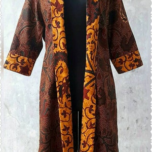 Op de afbeelding: Een lange bruine en gouden kimono met een contrasterende gouden en rode geprinte rand. De kimono is open aan de voorkant en heeft een lange, vloeiende silhouet.