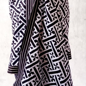 Puede incluir: Sarong con estampado geométrico en blanco y negro. El sarong está atado a la cintura y tiene un extremo largo y fluido.