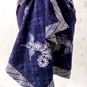 Puede incluir: Un sarong azul y blanco con estampado y borde blanco. El sarong está atado a la cintura y tiene un diseño floral.