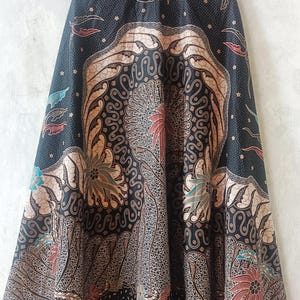 May include: A long, flowing skirt with a black background and a detailed batik pattern. The design features floral and abstract motifs in shades of brown, red, and blue. The text "LKG+" is visible at the top.