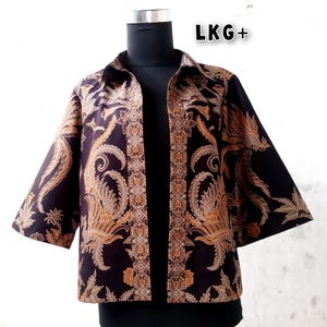 May include: A black and gold patterned jacket with a collar and three-quarter sleeves. The jacket features a floral design with a bird motif. The text "LKG+" is visible in the top right corner of the image.