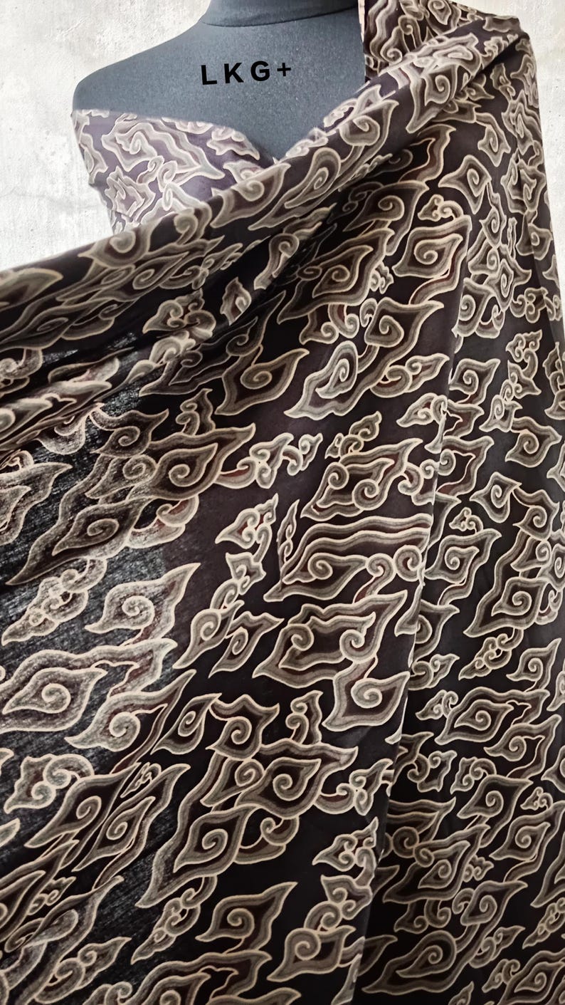 May include: Black fabric with a beige cloud-like pattern. The fabric is draped over a mannequin with the text "LKG+" on the chest.