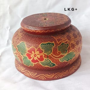 May include: A wooden bowl with a floral design in red, green, and yellow. The bowl has a raised rim and a small hole in the center of the top.