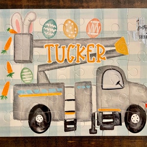 May include: A gray and yellow toy truck with a lift, decorated with Easter eggs and carrots. The truck has the name "TUCKER" written on it.