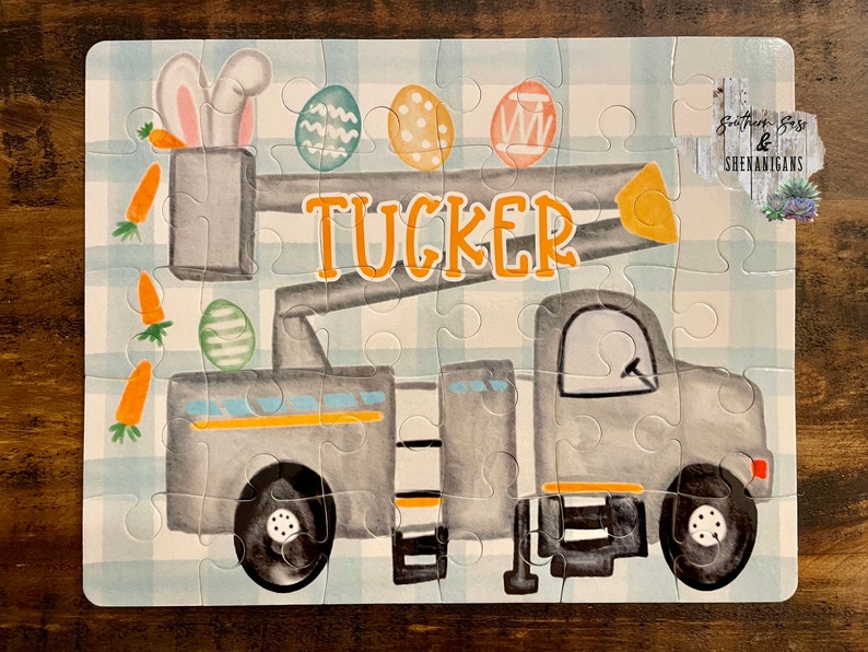 May include: A gray and yellow toy truck with a lift, decorated with Easter eggs and carrots. The truck has the name "TUCKER" written on it.