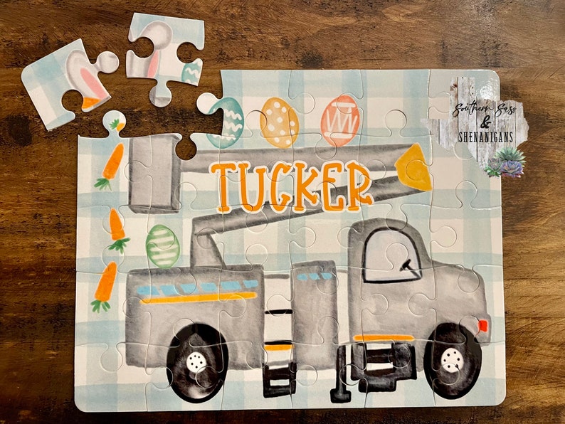 May include: A gray and yellow toy truck with a lift, decorated with Easter eggs and carrots. The truck has the name "TUCKER" written on the side. The puzzle is on a blue and white checkered background.