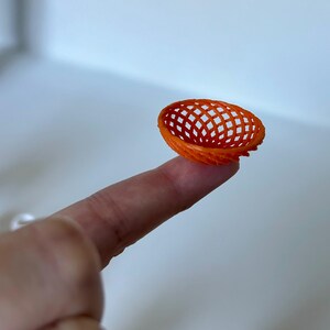 May include: A small, orange, plastic basket with a woven design. The basket is being held by a finger.