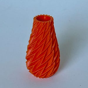 May include: A small, orange, 3D printed vase with a geometric, textured design.