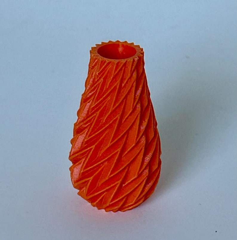 May include: A small, orange, 3D printed vase with a geometric, textured design.