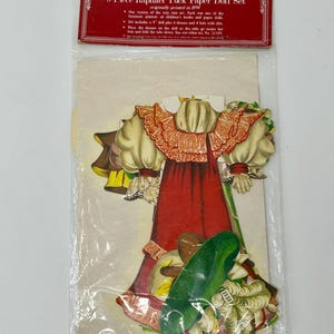 Puede incluir: Un conjunto de muñecas de papel vintage de 9 piezas que incluye un vestido rojo, un sombrero verde y otros accesorios. El conjunto está empaquetado en una bolsa de plástico transparente con una etiqueta roja y blanca que dice "Collector's Old-Fashioned 9 Inch 9-Piece Raphael Tuck Paper Doll Set originally printed in 1894".