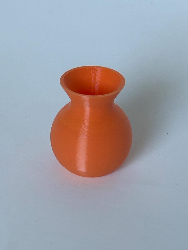 May include: A small, orange ceramic vase with a rounded body and a slightly flared opening.