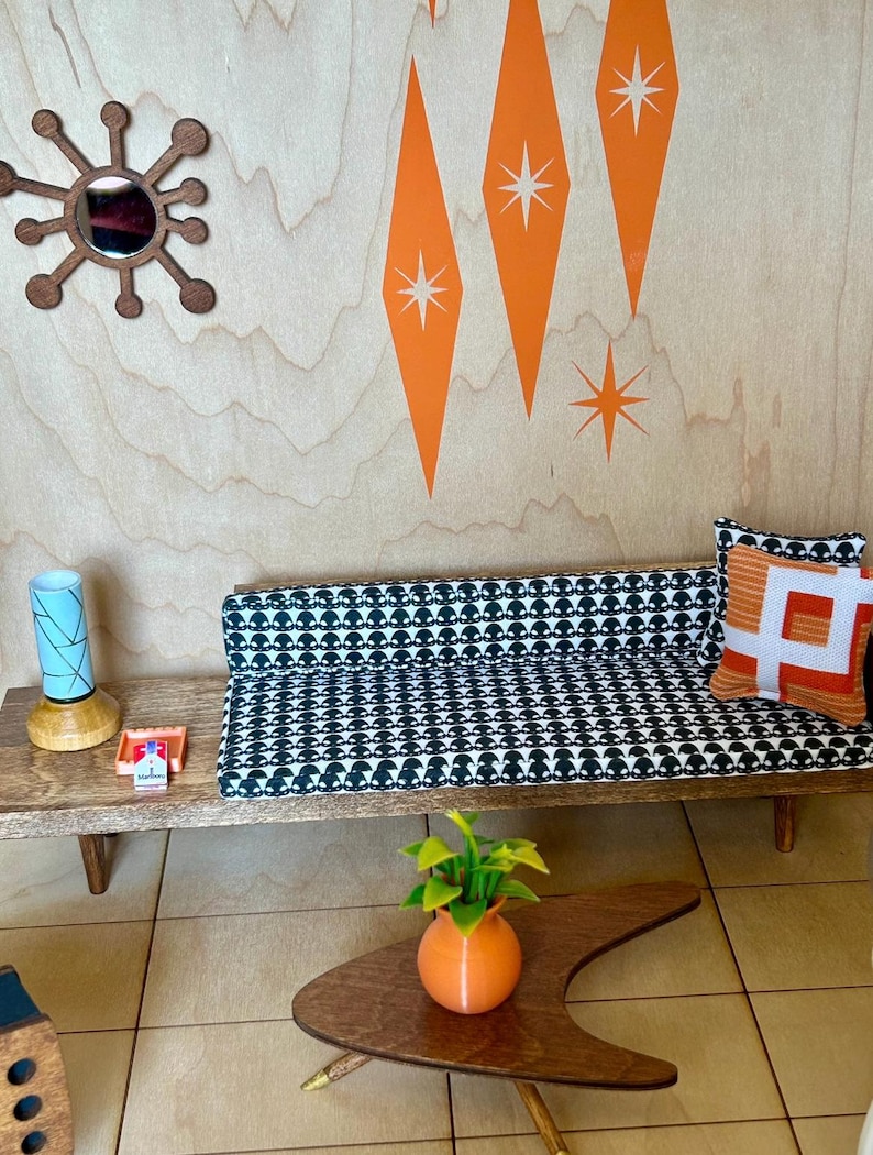 May include: A miniature mid-century modern living room set with a black and white patterned sofa, a wooden coffee table, a lamp, and a potted plant. The wall is decorated with orange diamond shapes and white stars.