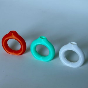 May include: Three small ceramic vases in red, turquoise, and white. Each vase has a round opening at the top and a rounded, ring-like base.