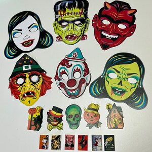 May include: A collection of vintage-style Halloween decorations. Includes masks of a vampire, Frankenstein's monster, a devil, a witch, a clown, and a zombie. Also features small cutouts of a cat, a skull, a pumpkin, a haunted house, and vintage Halloween cards.