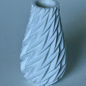 May include: A white ceramic vase with a textured, geometric design. The vase has a narrow opening and a wide base.