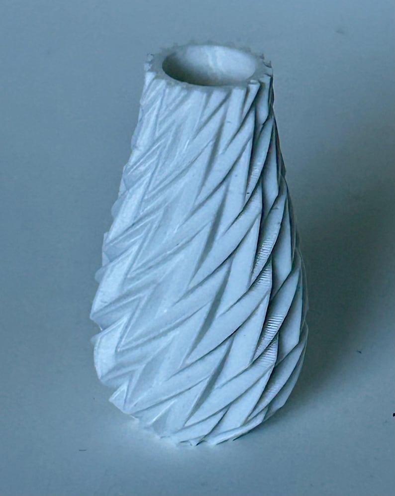 May include: A white ceramic vase with a textured, geometric design. The vase has a narrow opening and a wide base.